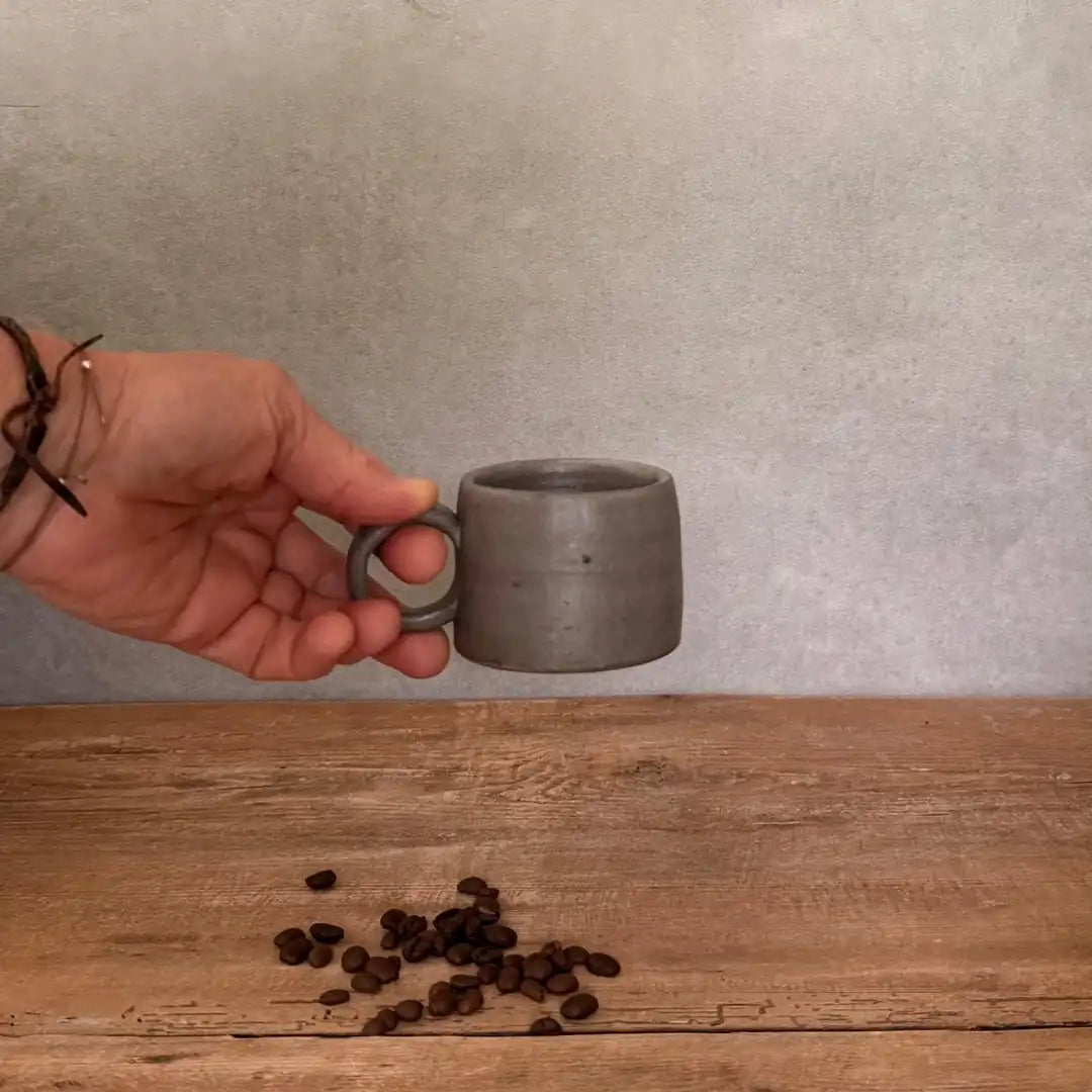 Hand hält AREIA Natural EspressoBecher am Henkel, freigestellt vor Wand