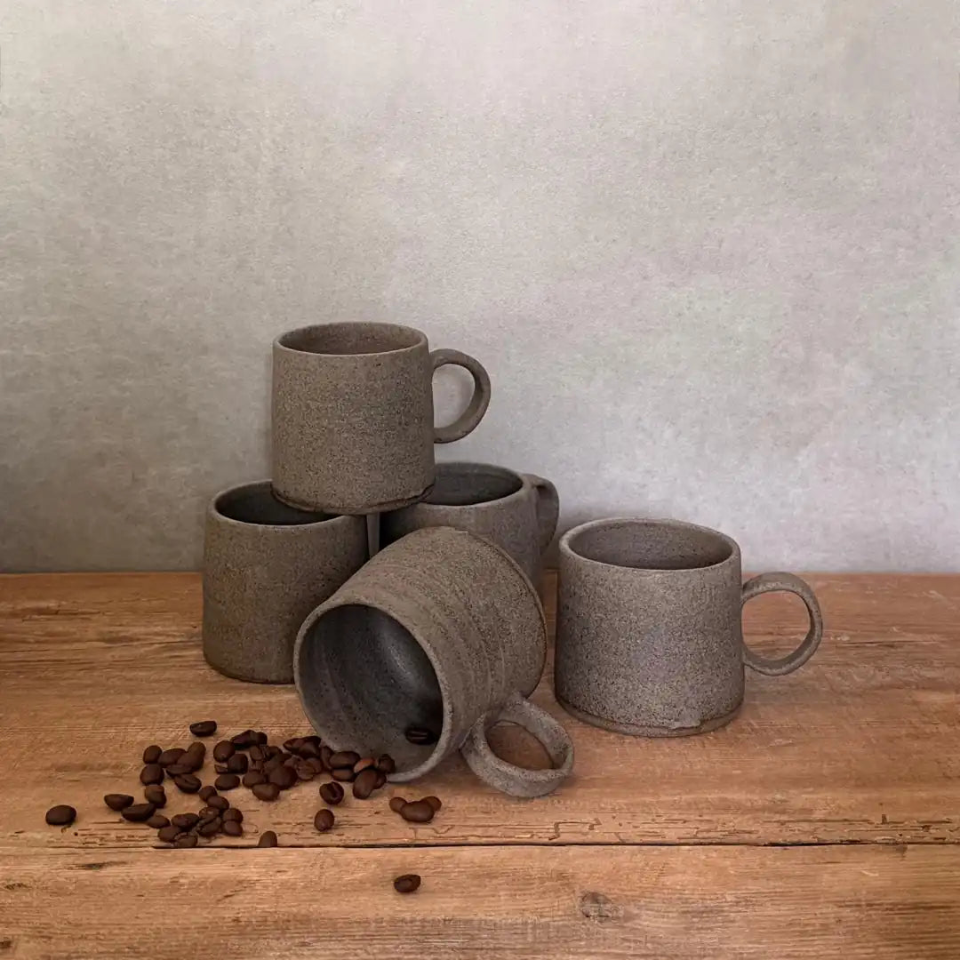 AREIA Cappuccino-Tasse in Salt & Pepper liegend mit Kaffeebohnen im Innenraum