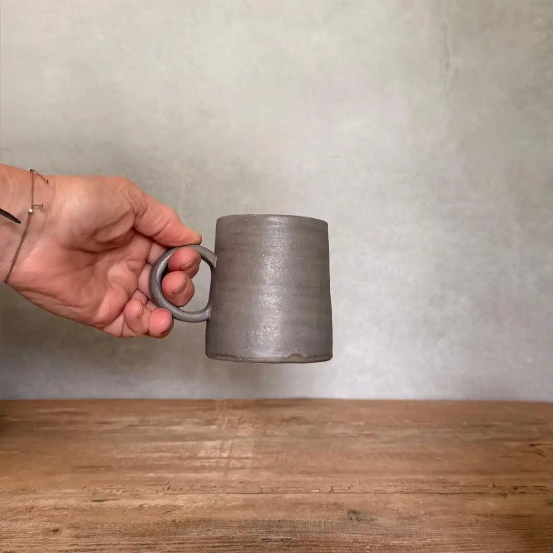 Hand hält AREIA Natural Tee Becher am Ringhenkel hoch