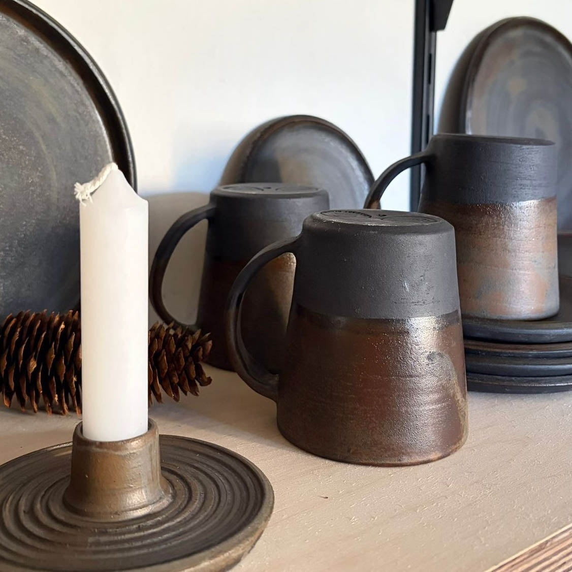 AREIA Negra Kaffeebecher auf dem Kopf stehend, im Vordergrund Kerzenständer, dunkler Steinzeugton mit brauner oldfinished Glasur, handgemacht