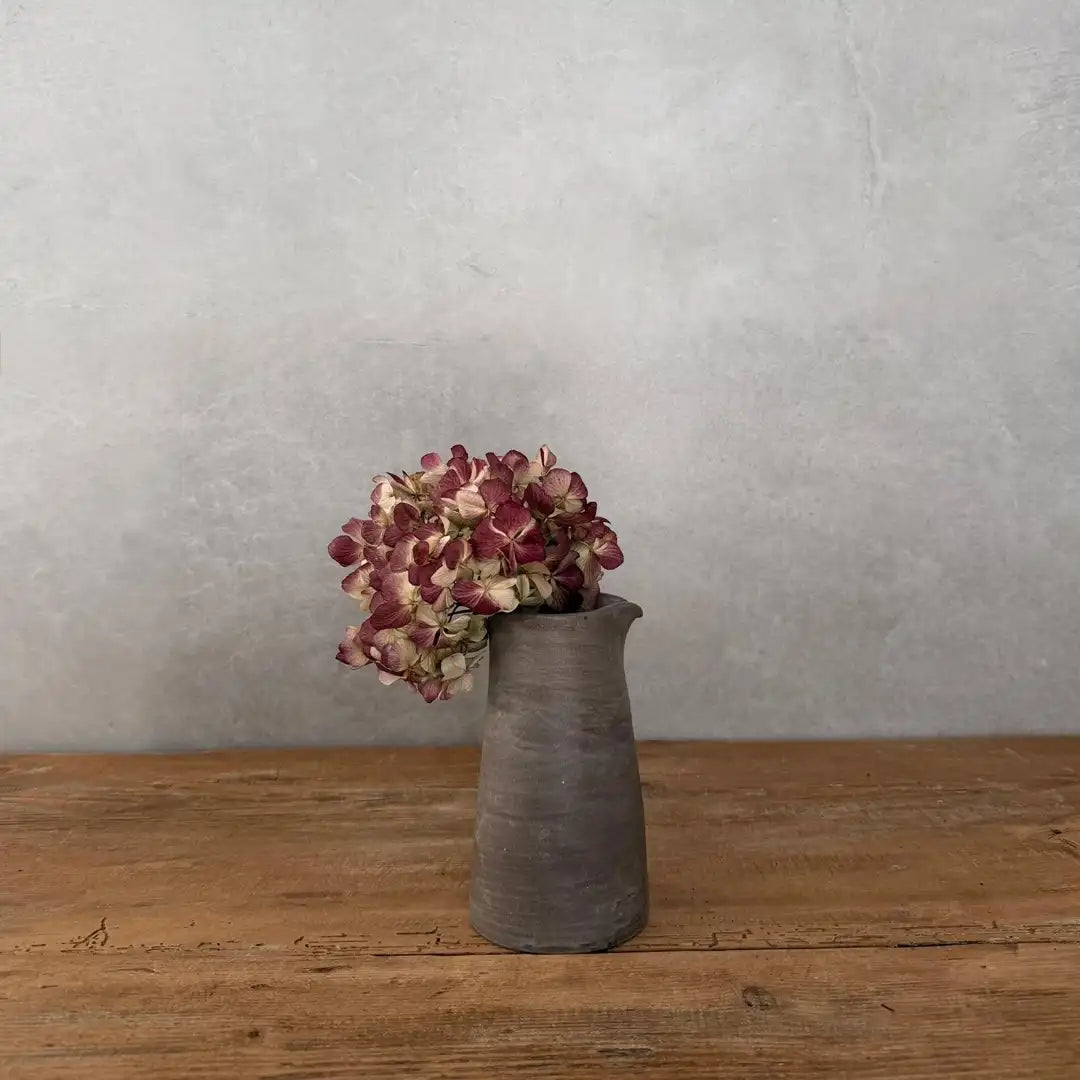 AREIA Natural Vase/ kleiner Krug mit Trockenblumen, auf Holztisch vor grauem Hintergrund
