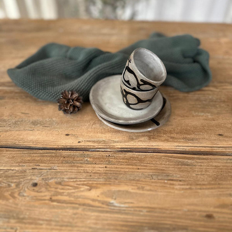 Handgemachtes Keramik-Set Black Snake auf einem Tisch, bestehend aus Becher und Tellern.
