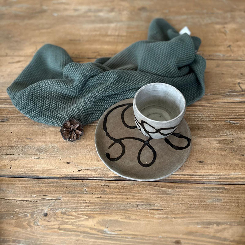 Detail der schwarzen Glasur-Schlangenlinie auf grauem Teller mit transparenter Glasur, handgefertigtes Becherset