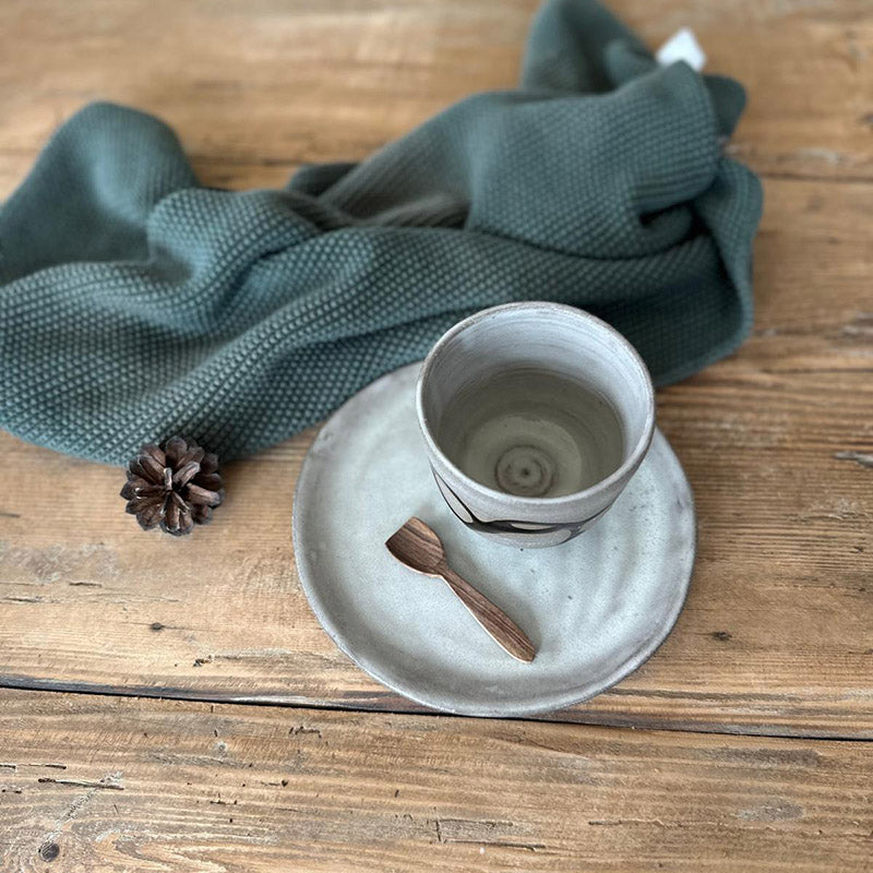 Handgemachtes Keramik-Set Black Snake, Tasse und Teller auf Holztisch mit Löffel und grünem Tuch.