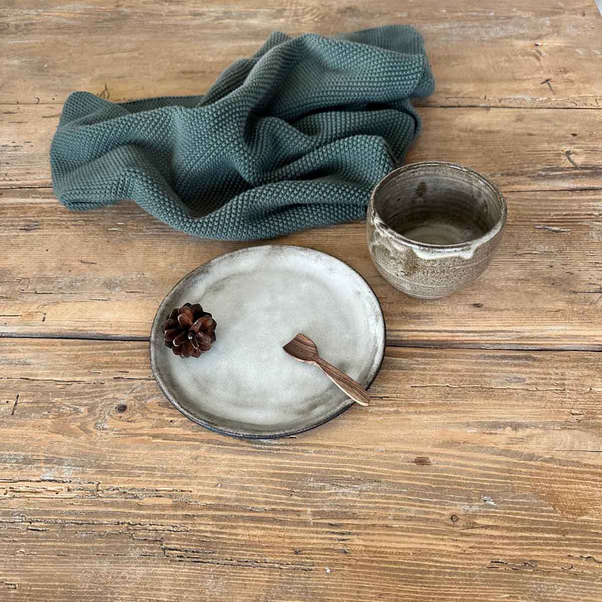 Braun-weiß glasierter Becher aus Steinzeug auf minimalistischem, weiß glasiertem Teller als Geschenkset