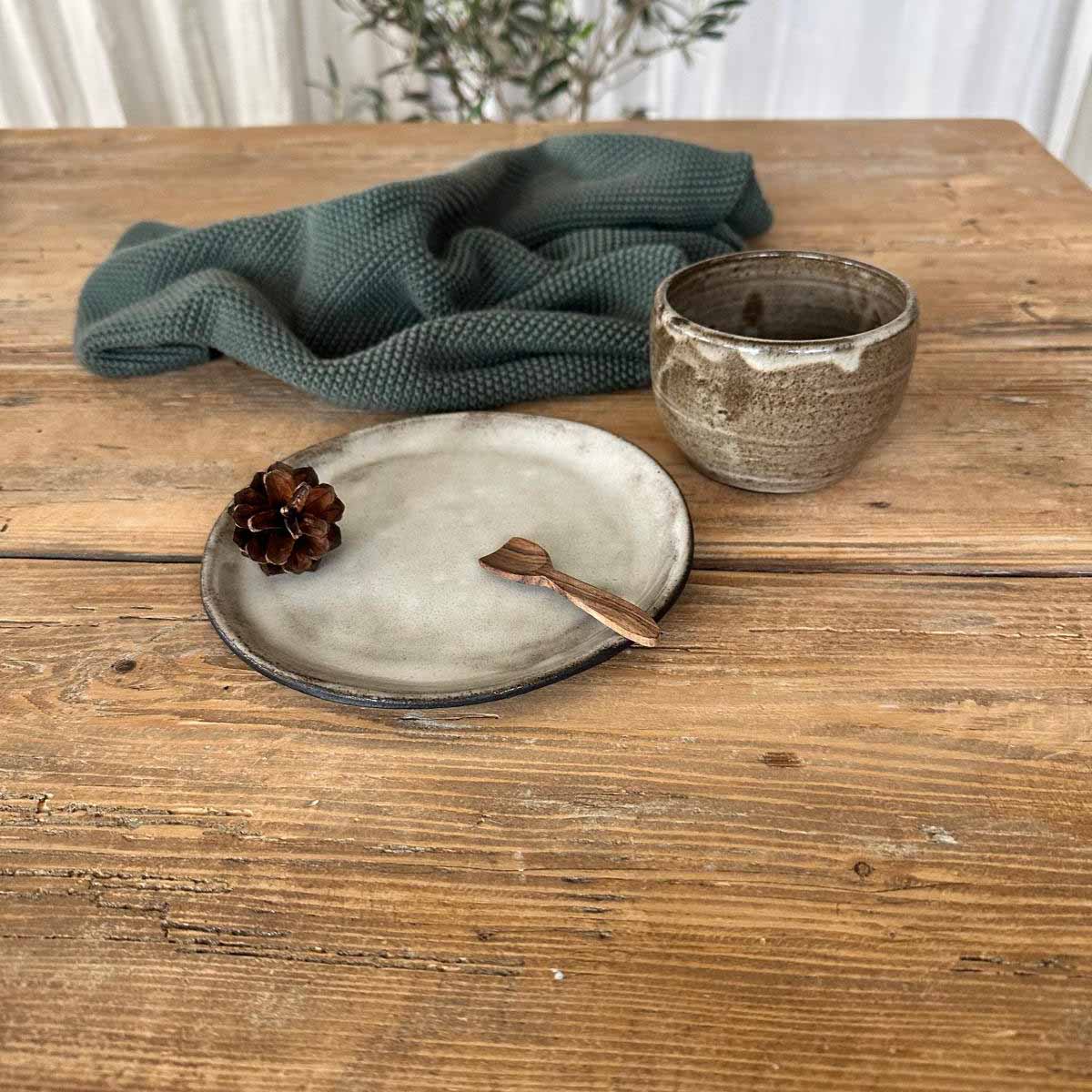 Detailansicht des dickwandigen Bechers mit lebendiger braun-weißer Glasur auf weißem Keramikteller