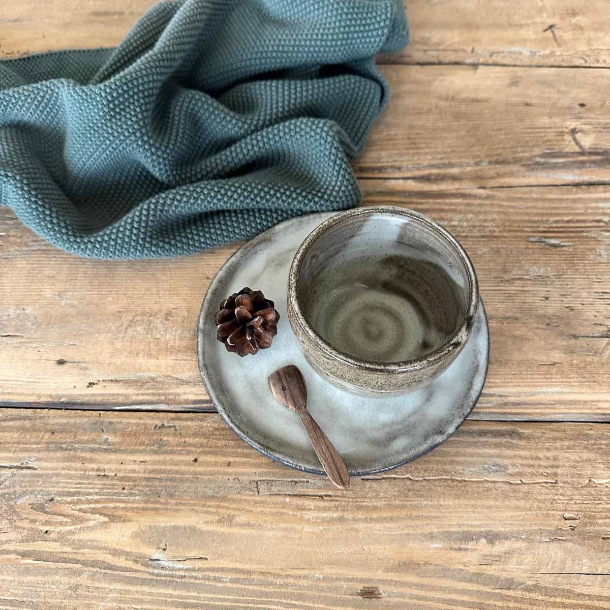 Handgemachtes Becherset, braun-weißer Becher und rein weiß glasierter Teller, arrangiert auf Holztisch