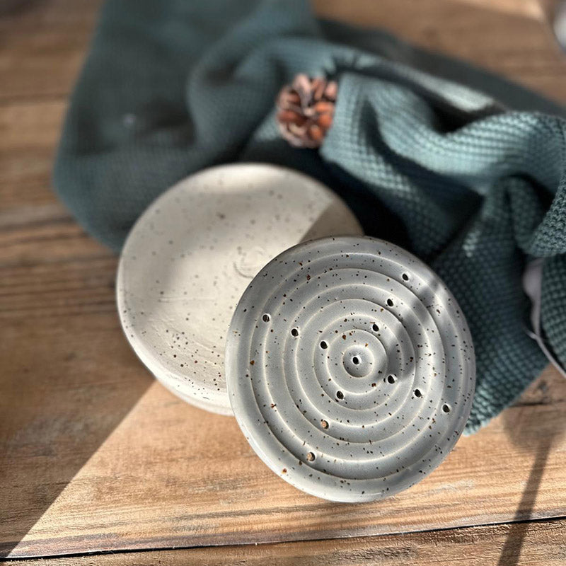 Runde graue Seifenschale mit Spots, dezente Bad-Deko neben strukturiertem Tuch, Affangschale umgedreht, Oberschale mit Rillen und Ablauflöchern