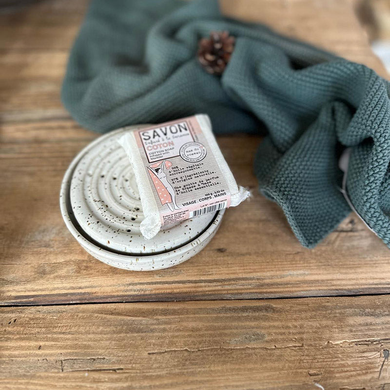 Runde weiße Keramik-Seifenschale mit Sprenkeln und verpackter Seife auf Holztisch