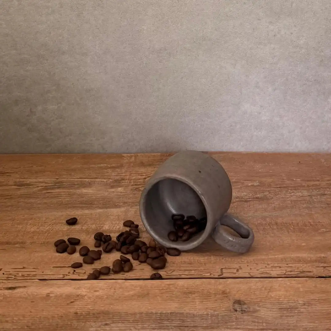 AREIA Natural EspressoBecher einzeln auf Holztisch liegend mit Kaffeebohnen, schlichte Produktansicht
