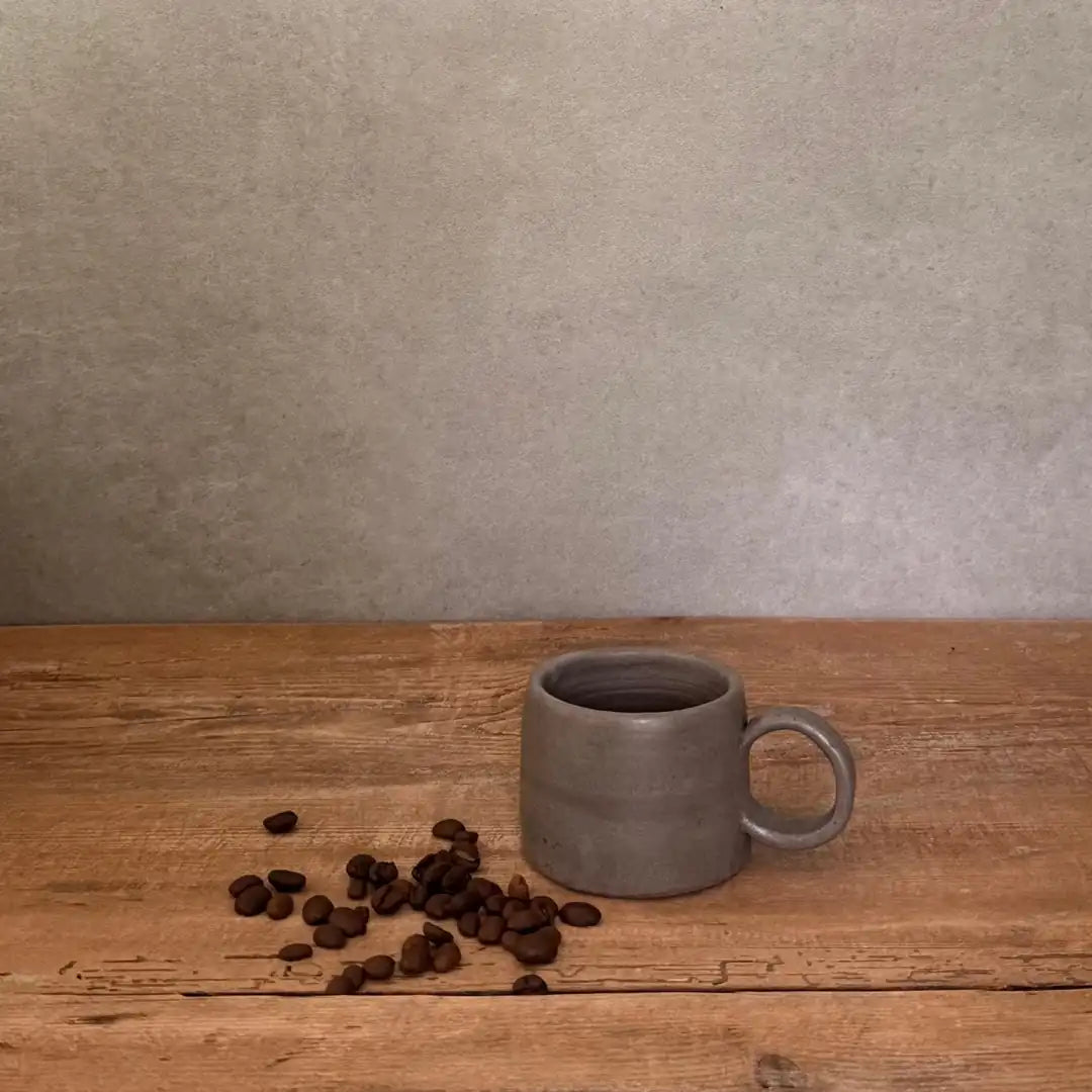 AREIA Natural EspressoBecher einzeln auf Holztisch mit verstreuten Kaffeebohnen, schlichte Produktansicht