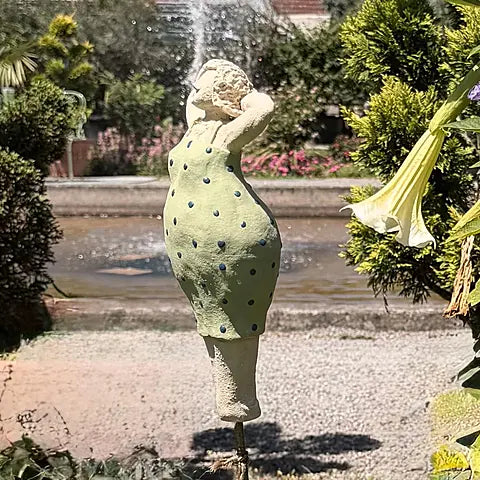 Keramikfigur in grün-gepunktetem Kleid vor Springbrunnen, Rückansicht mit Armen am Kopf