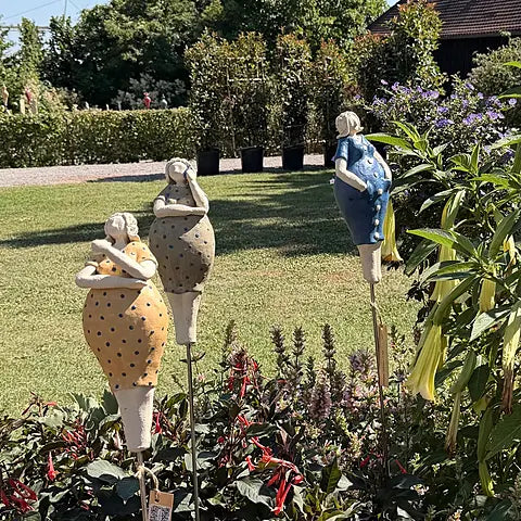 Drei Keramikfiguren im Garten – gelb und grünes Kleid mit Punkten und blaues Kleid mit weißer Knopfleiste, Frontalansicht