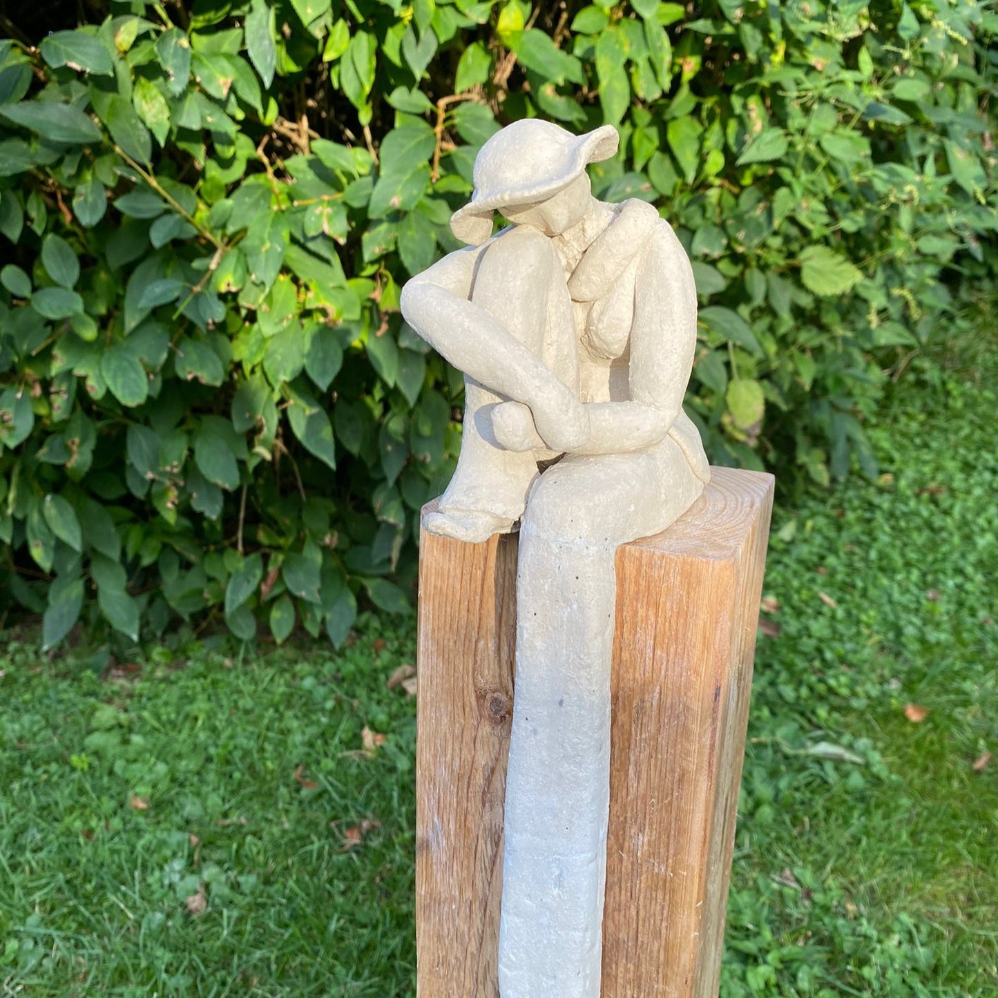 Sitzende Dame mit angezogenem Fuß aus weißem Ton auf einem Ständer aus Altholz.