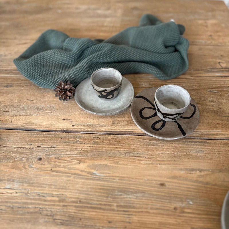 Espresso-Duo aus Steinzeug mit zwei kleinen Bechern und Tellern, eines mit Schlangenlinie, eines weiß glasiert