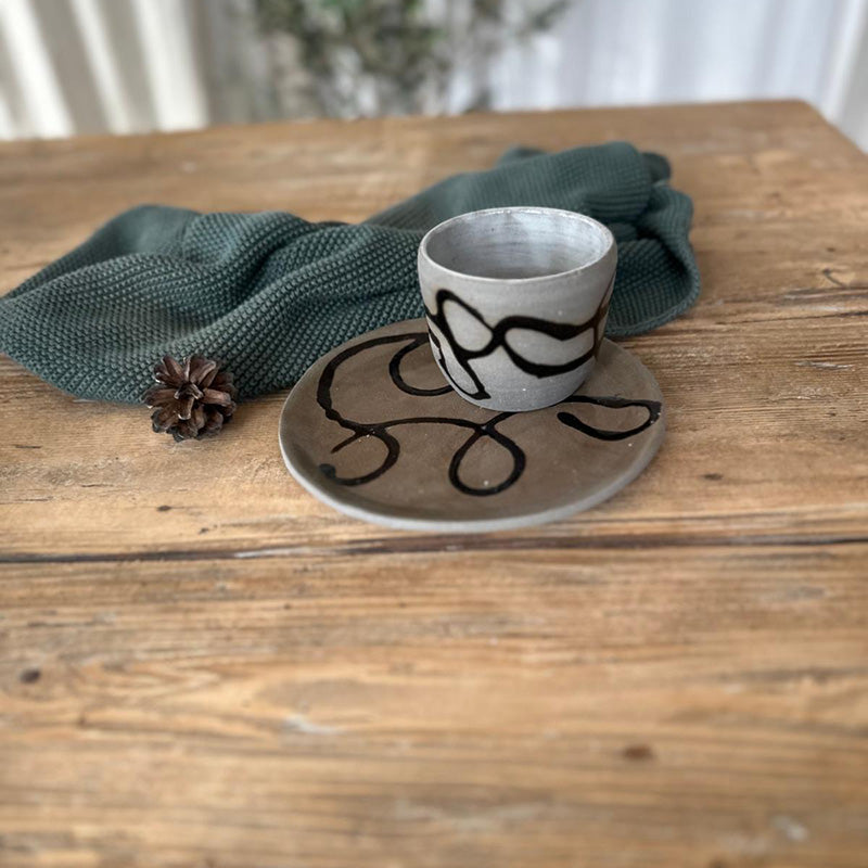 Becherset aus grauem Steinzeug mit schwarzer Schlangenlinie auf Teller und Becher, handgemacht von FRANZART Keramik