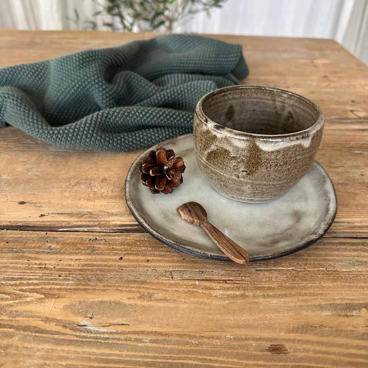 Nahaufnahme des braun-weißen Bechers, der Teller darunter ist glatt weiß glasiert