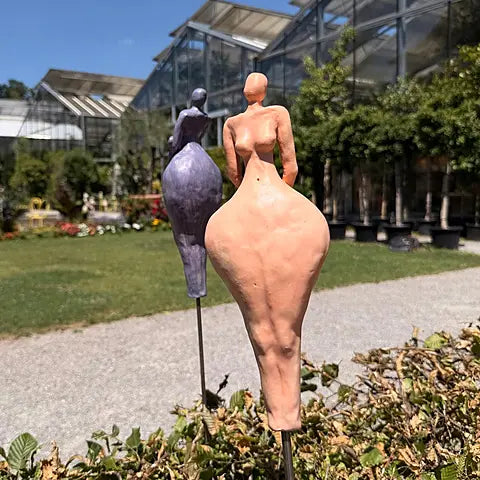Keramikfiguren in gelborange im Vordergrund und in Fliederfarben im Hintergrund, abstrakte weibliche Silhouetten auf Steinterrasse​​​​​​​​​​​​​​​​
