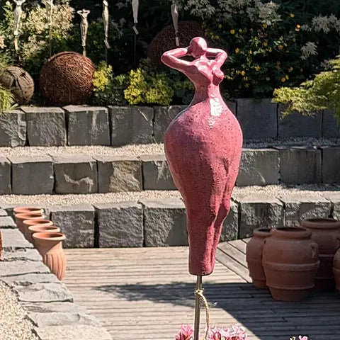 Keramikfigur in Rot auf Terrasse, abstrakte weibliche Silhouette mit erhobenen Armen, zwischen Terrakottatöpfen
